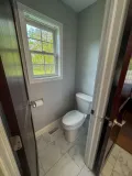 Brightly lit bathroom featuring a modern toilet, marble flooring, and a window overlooking greenery outside.